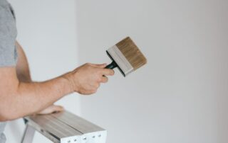 A man on top of a ladder holding a wide flat brush, Sustainable Paint Disposal Methods, painting walls white